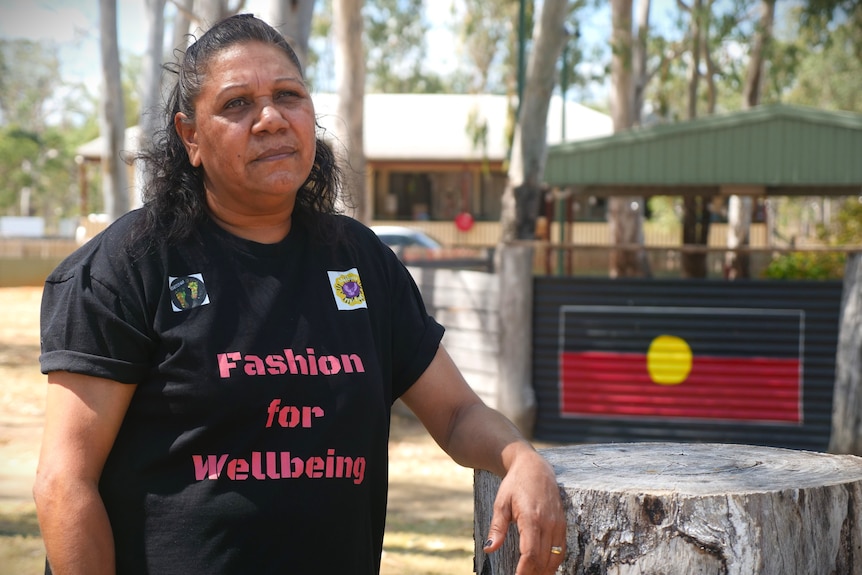 A woman leans her arm on a tree stump in front of a painting of the Aboriginal flag.