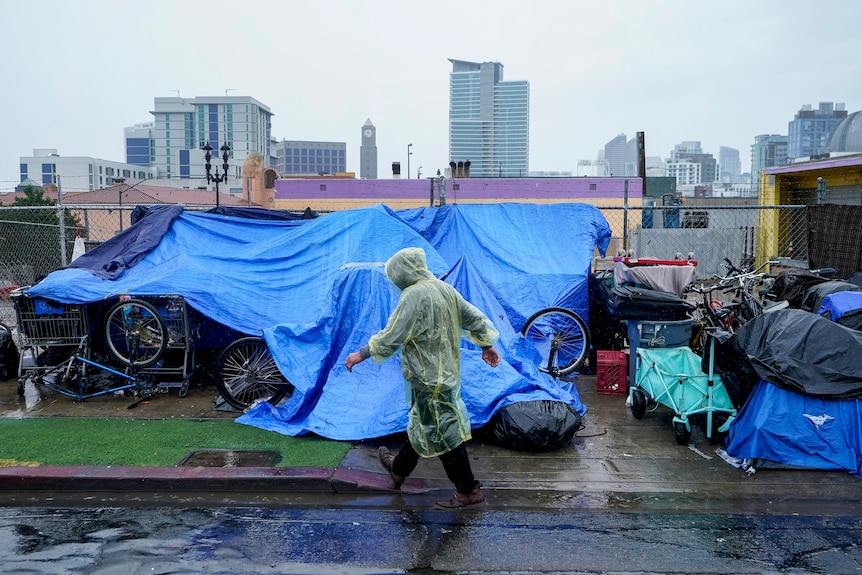 A person wearing a rain poncho walks past things covered in tarpaulin