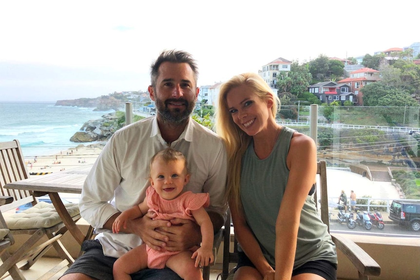 Ben and Brittan Guthridge holding their daughter Mackenzie at a location overlooking the coastline.