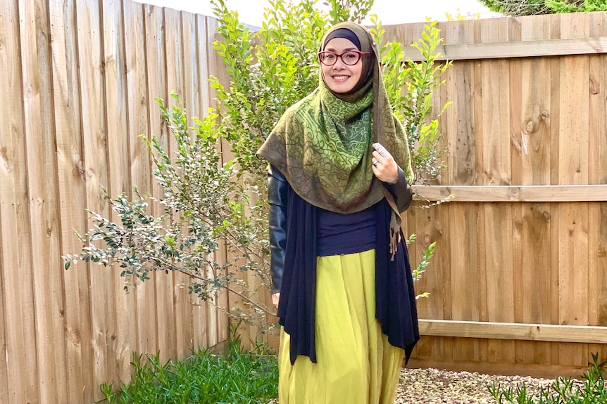 A woman standing in front of a tree in a her backyard.