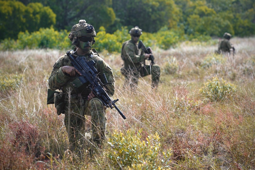 Soldiers in battle dress and camouflage take a knee while on patrol as part of a training exercise in Queensland.