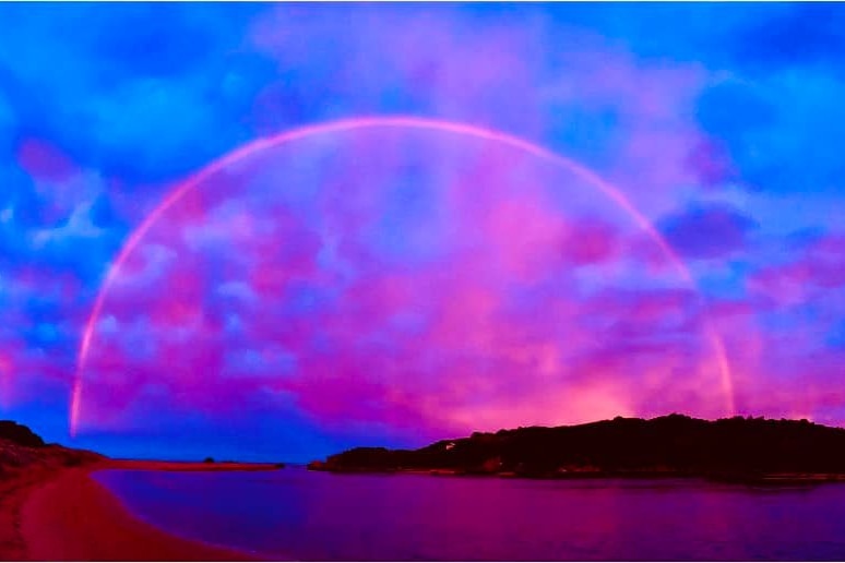 Fluorescent rainbow and sunset over lake and ocean.