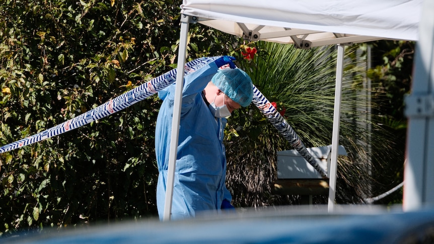 A police officer in a HAZMAT suit lifting up police tape. 