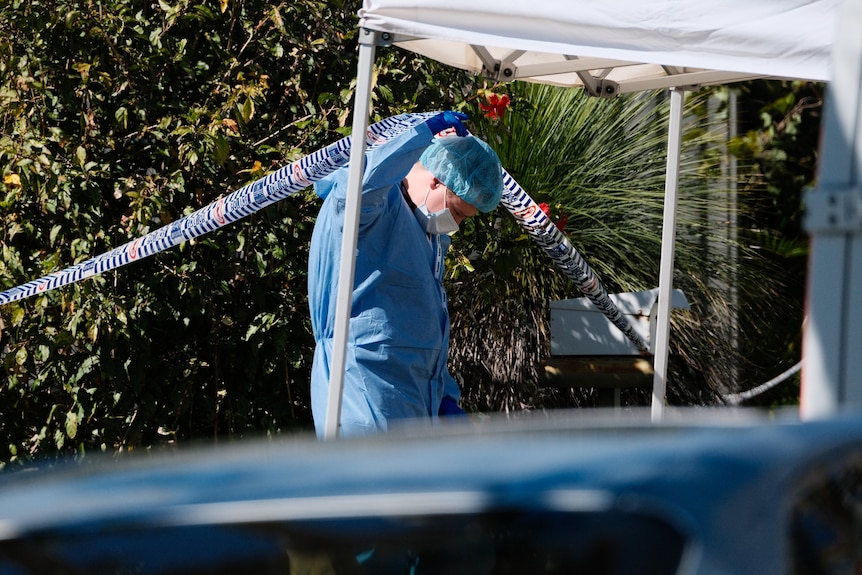 A police officer in a HAZMAT suit lifting up police tape. 