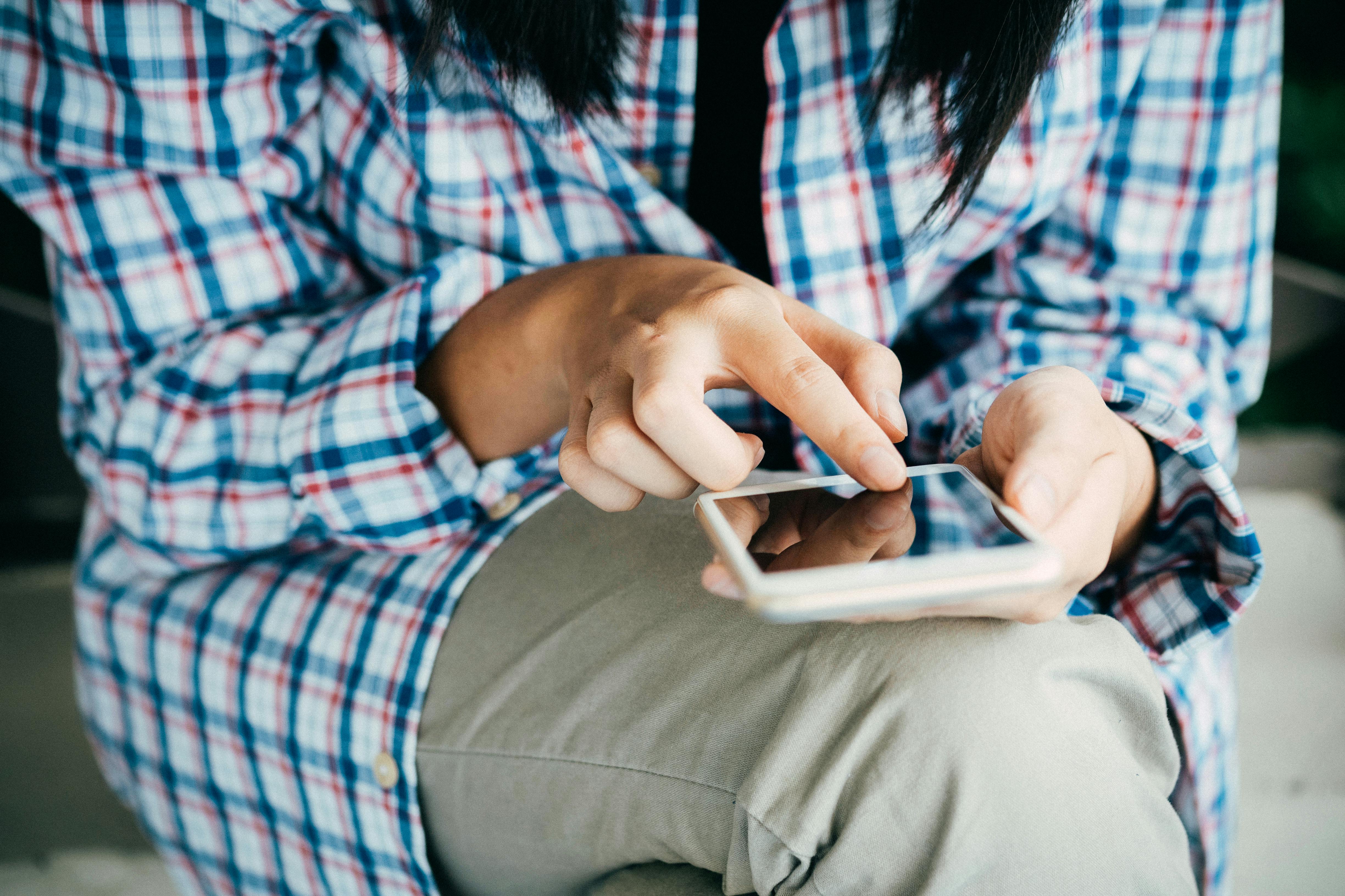 close up of woman in blue check shirt looking at mobile phone
