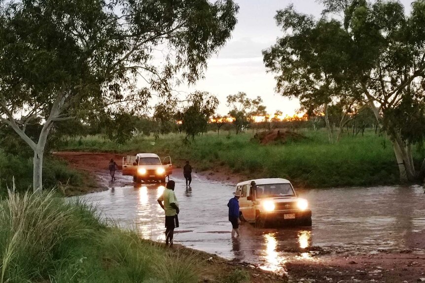 A mid range shot of a 4WD coming out of a flooded red dirt road at dusk