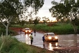 A mid range shot of a 4WD coming out of a flooded red dirt road at dusk