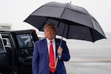 Man in blue suit and red tie holds umbrella. 