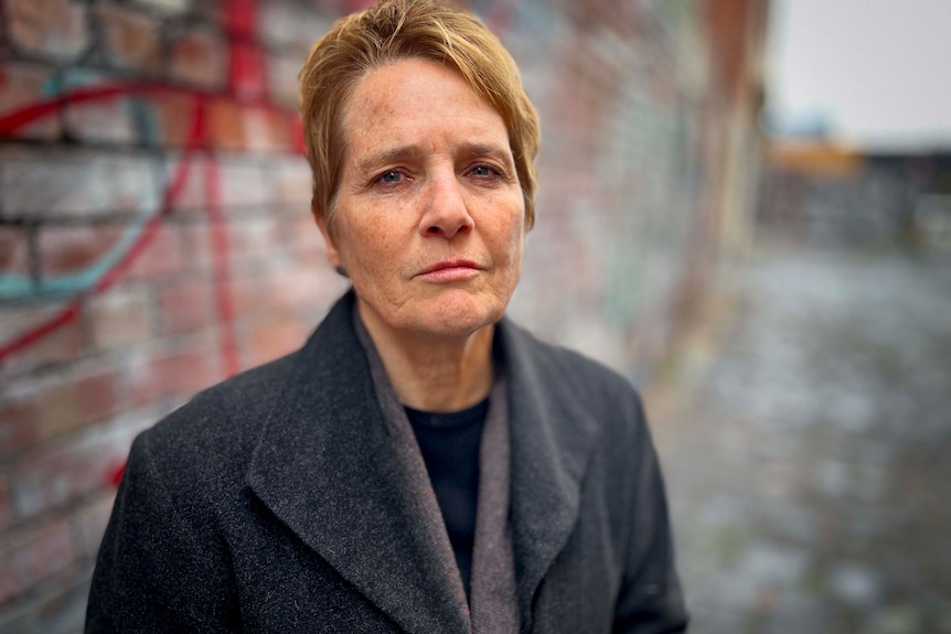 A woman in an alley way with short blonde hair and a jacket