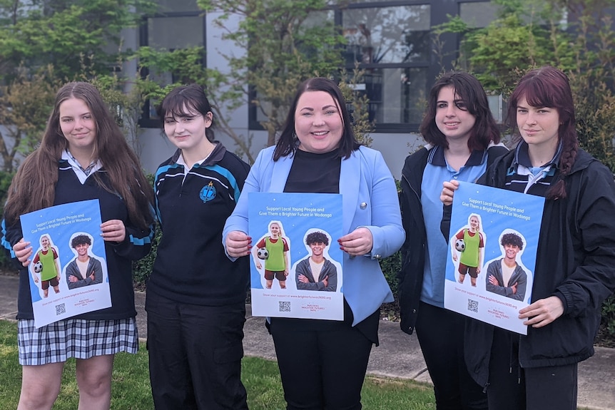 Four students in school uniforms stand with a woman in a blue blazer, holding posters for the Building Brighter Future Project