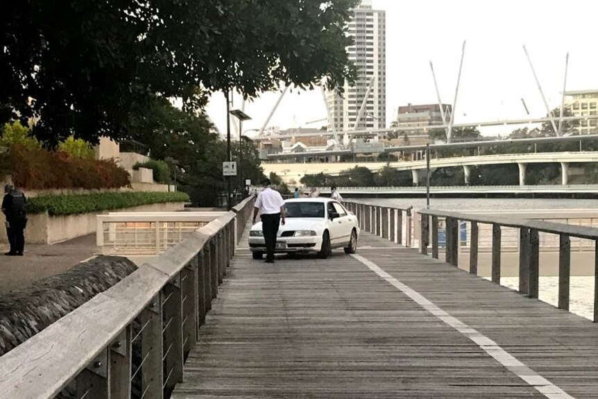 Security guard inspects a car which had been driven down a boardwalk along the Brisbane River.