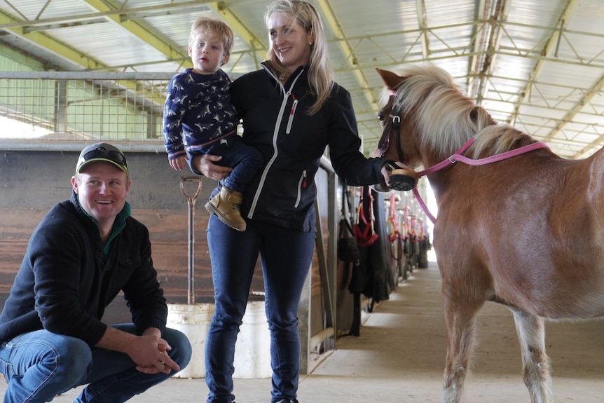 A man and woman stand with their young child next to a horse.