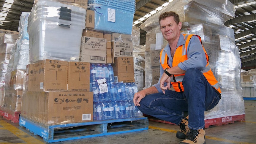 LINFOX Townsville warehouse manager Michael Power crouches down in front of pallets of supermarket goods