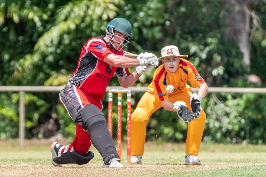 Lochie Hardy plays a sweep shot during a cricket game in Darwin while the wicket keeper crouches at the ready..