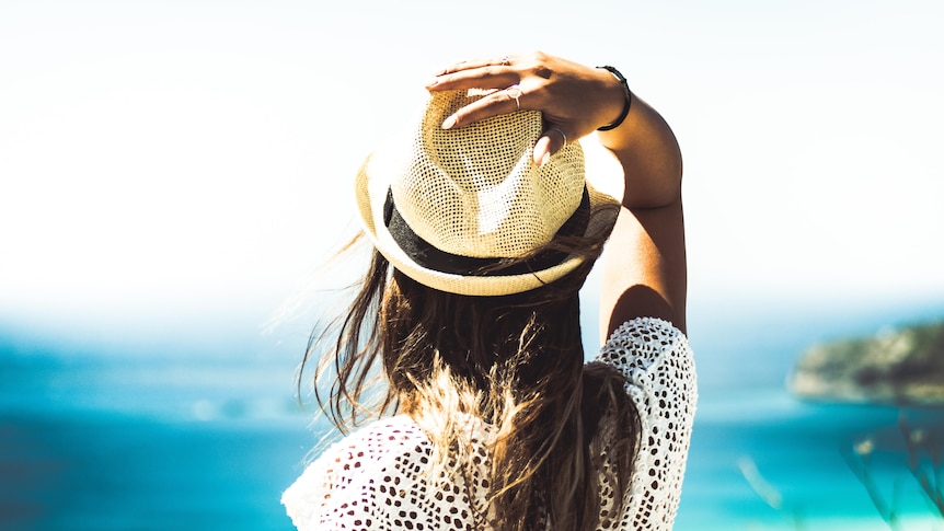 Woman holding her hat and gazing at the ocean horizon in a story about making the most of summer amid coronavirus