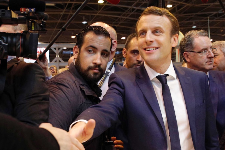 Alexandre Benalla stands between French President Emmanuel Macron and a media pack