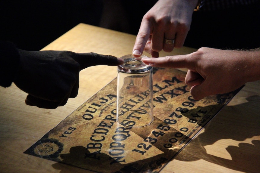 Unidentifiable people use a Ouija board.