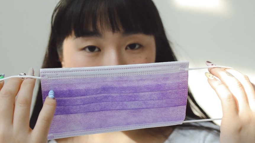 Woman holds a disposable mask in front of her face, a childcare worker during the coronavirus pandemic.