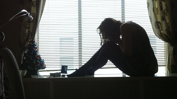 A woman sitting near a window with her head on her knees.