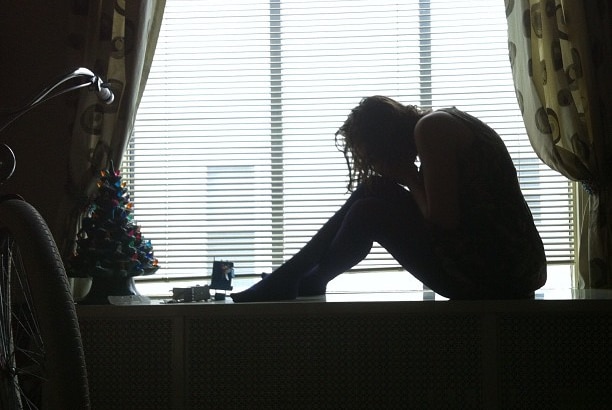 A woman sitting near a window with her head on her knees.