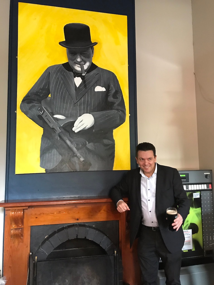 Nick Xenophon stands in front of a giant portrait of Sir Winston Churchill.