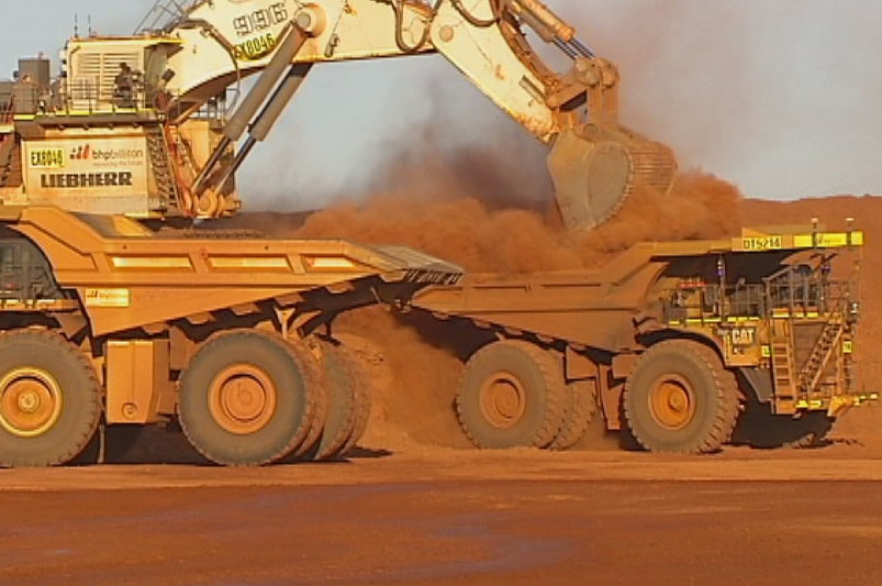 A digger loads autonomous trucks with dirt at a Pilbara mine site