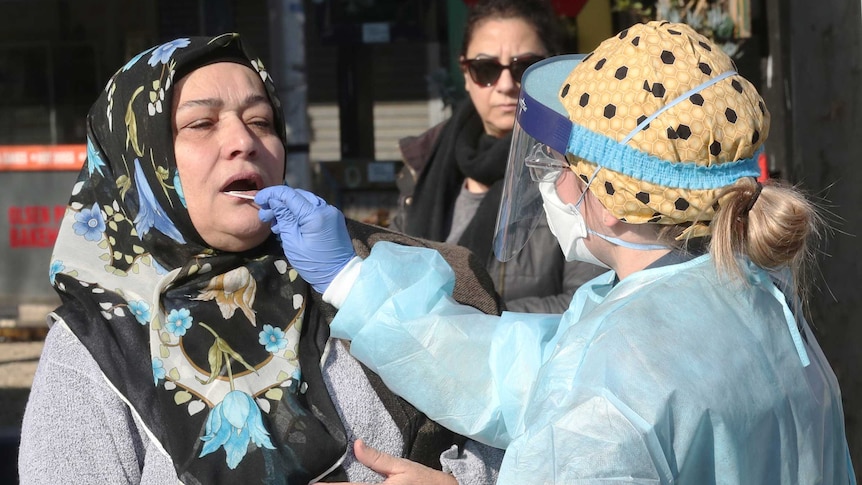 A woman has her mouth swabbed by a doctor for a COVID-19 test