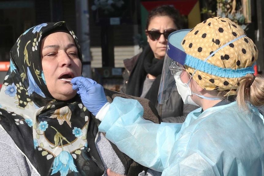 A woman has her mouth swabbed by a doctor for a COVID-19 test