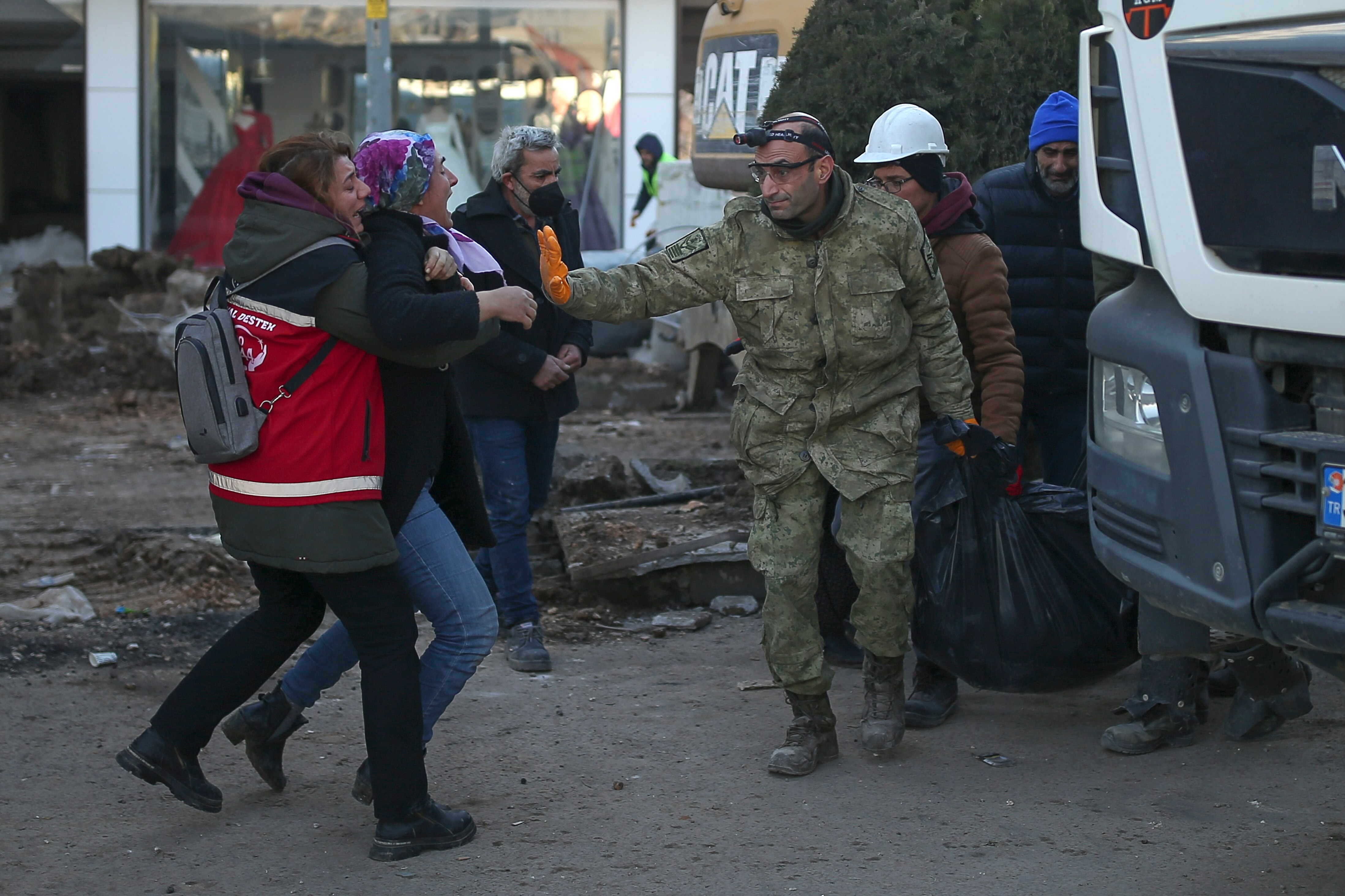 Two women cry out as a rescue worker holds his hand up to stop them while carrying a body bag.