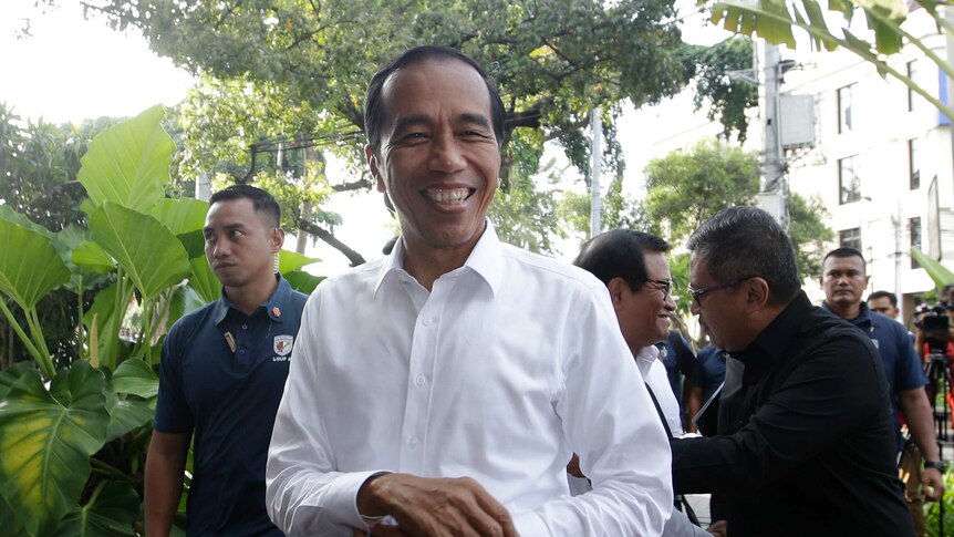 Indonesia's president Joko Widodo smiles in a while shirt, surrounded by security officials.