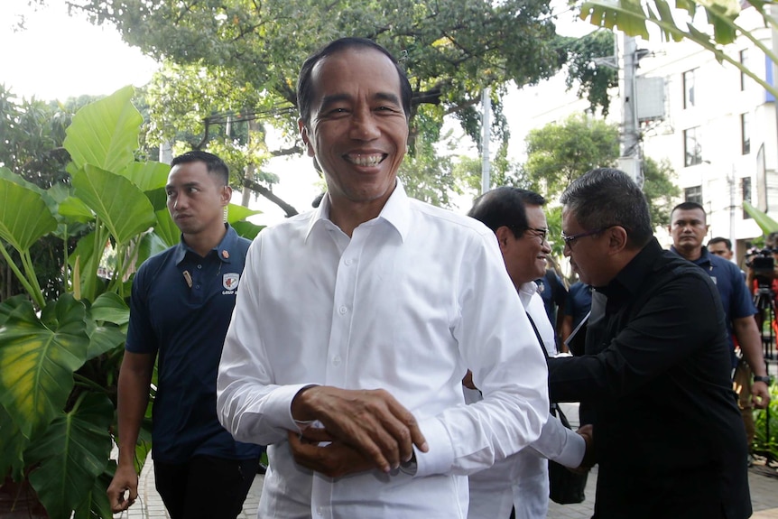 Indonesia's president Joko Widodo smiles in a while shirt, surrounded by security officials.