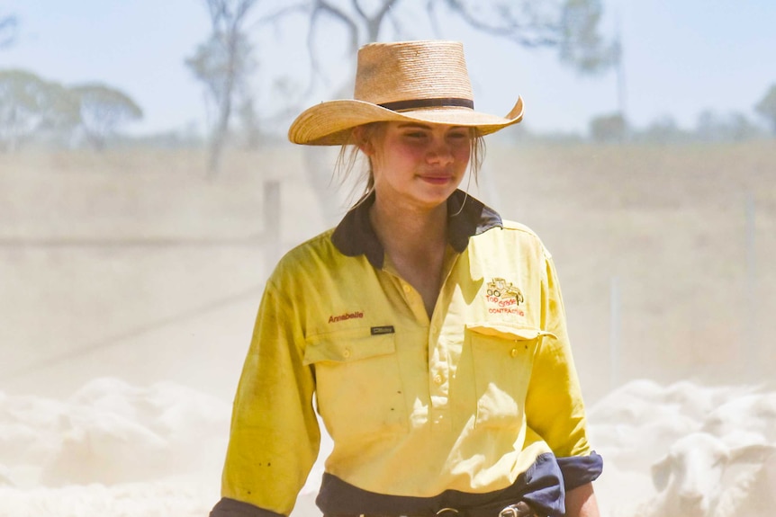 A teenage girl walks through a dusty holding cell of sheep