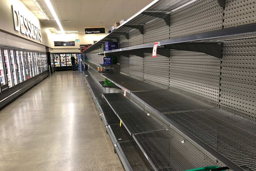 A supermarket with a large stretch of empty shelves.