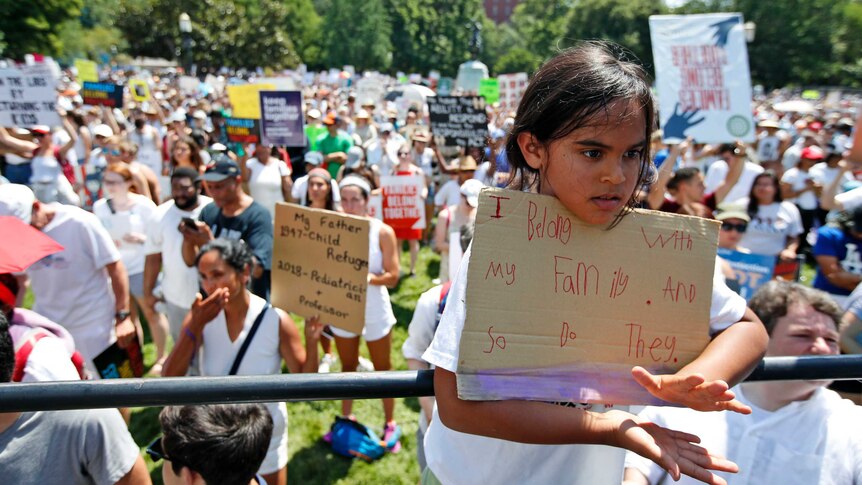 A young girl holds a sign saying 'I belong with my family and so do they.'