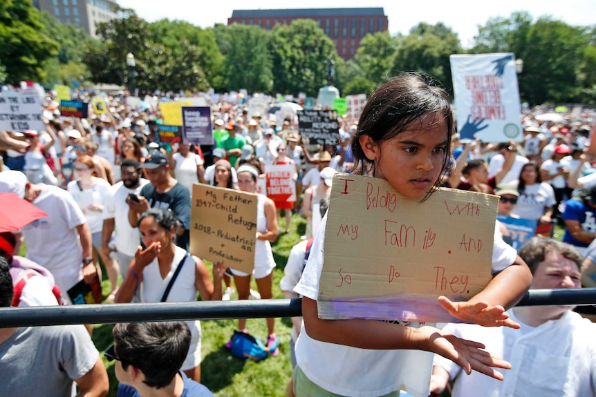 A young girl holds a sign saying 'I belong with my family and so do they.'