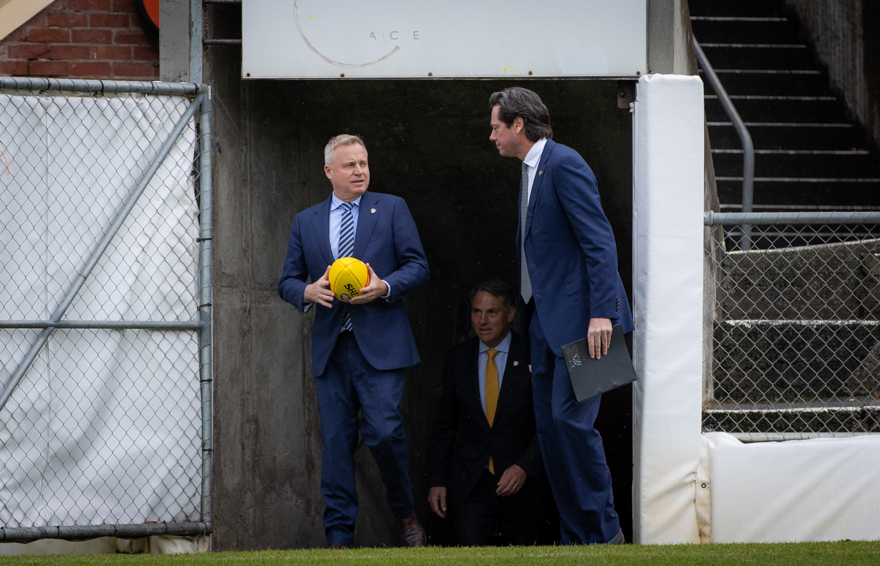 Two men in suits emerge from a tunnel at a football oval