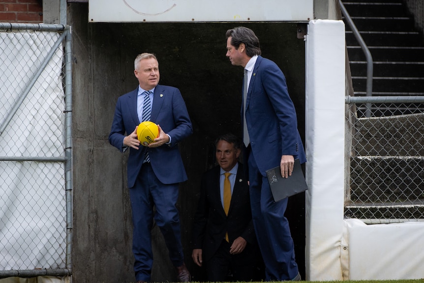 Two men in suits emerge from a tunnel at a football oval