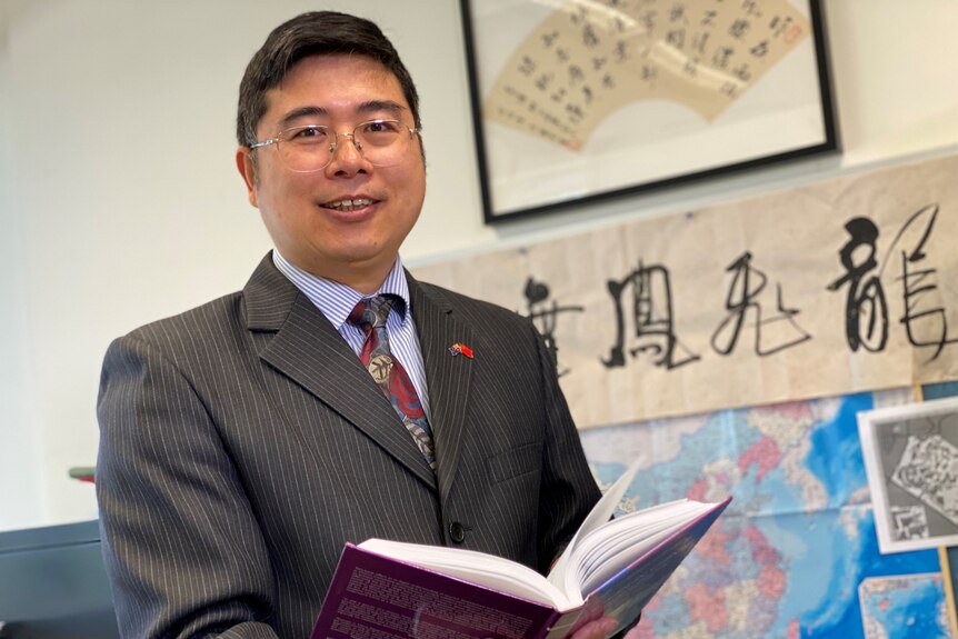 Sam Huang waring a suit holding a book. 