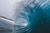 A shot from inside a barrel wave as it crashes near shore with the beach in the distance.