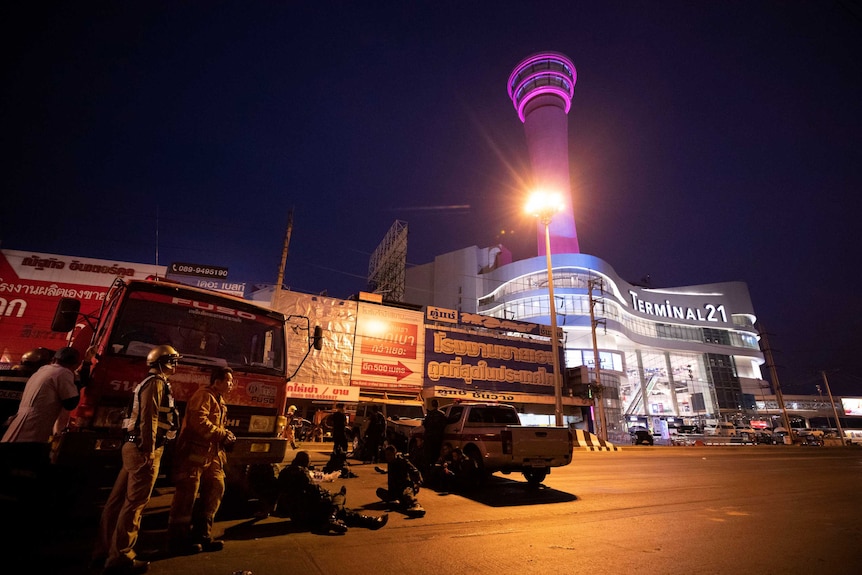 Emergency workers stand outside a large shopping complex in Thailand, at night.