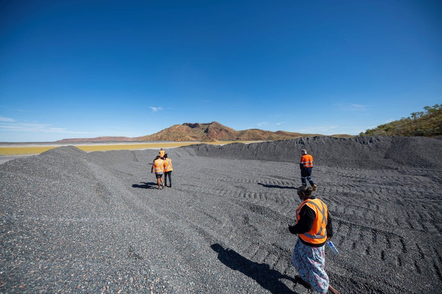 A group of people in high-vis vests walk in a large area of gravel.