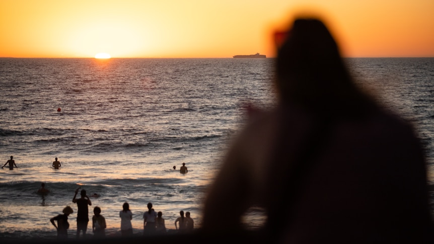 Members of the public at a crowded beach during sunset.
