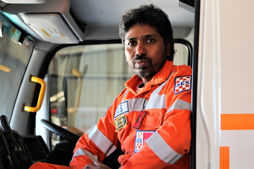 A man wearing a bright orange SES uniform sits in a truck and looks at the camera.