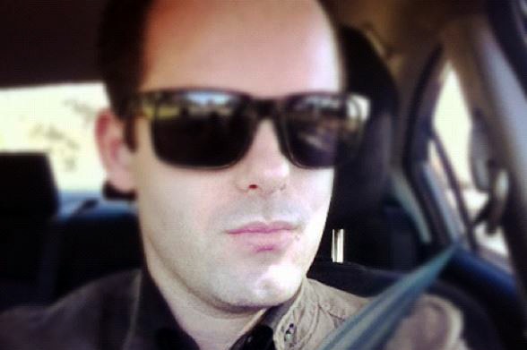 Mathew Reale wearing sunglasses and sitting behind the wheel of a car.