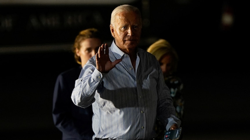 Joe Biden with one hand raised partially covered by dark shadows. 