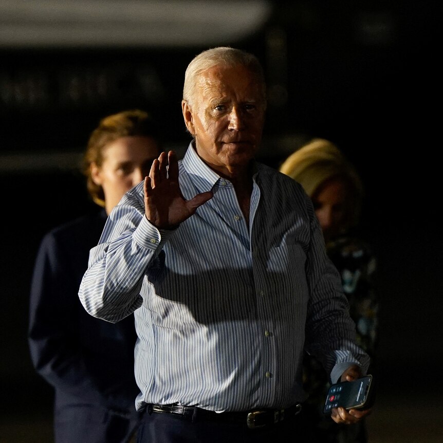 Joe Biden with one hand raised partially covered by dark shadows. 