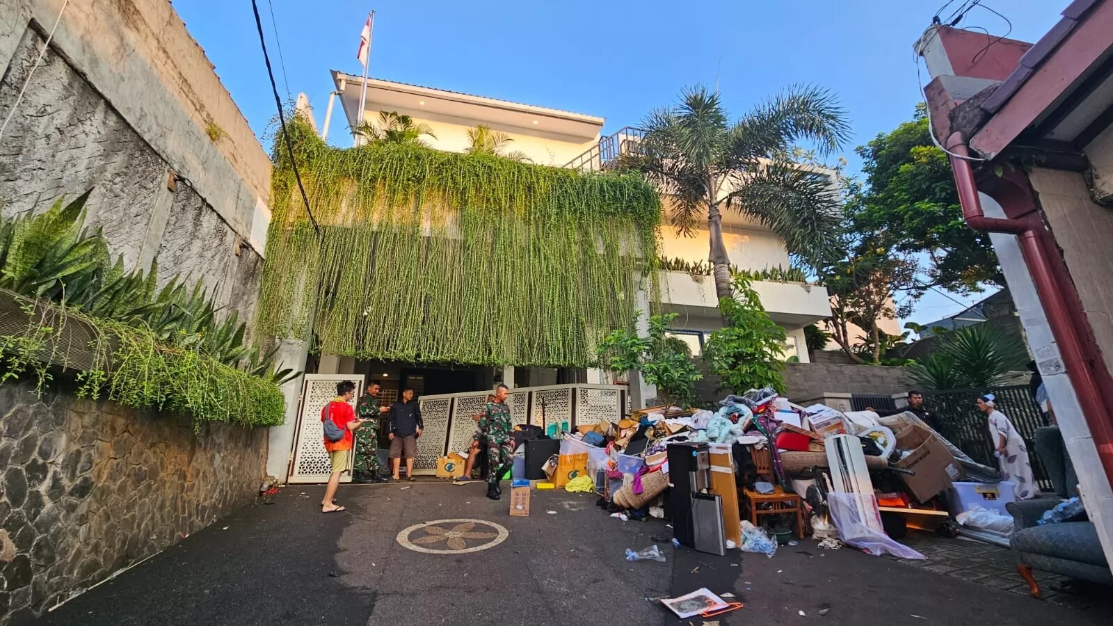 A pile of personal effects sits in front of a multi-storey house with green foliage over the front 