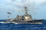 The USS Dewey warship conducts a vertical replenishment with helicopters flying about.