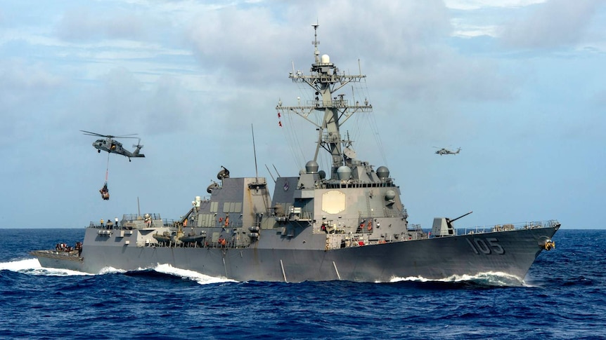 The USS Dewey warship conducts a vertical replenishment with helicopters flying about.