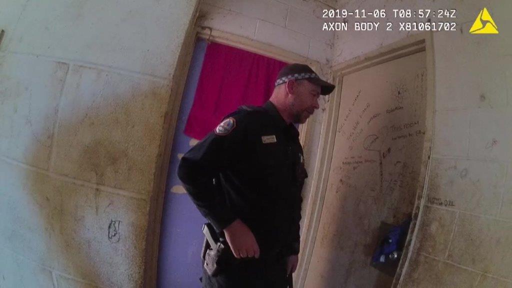 A NT Police officer can be seen in a screenshot from body-worn video. The officer is knocking on a door.